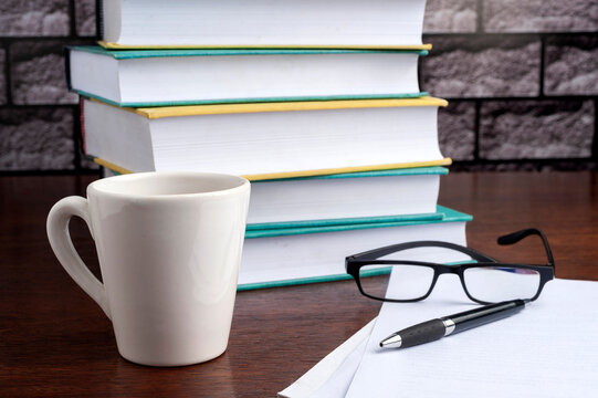 books on a desk with a cup of tea, blank sheets, glasses and a pen and a camera