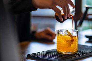 Asian woman barista pouring espresso shot on fresh orange juice in the glass. Female coffee shop waitress serving iced black coffee with orange juice on counter at cafe. Small business owner concept.