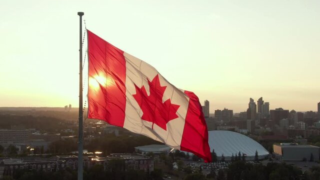Aerial orbiting shot showing Canada flag waving in the wind against the sun on Canada Day in Calgary, Alberta, Canada, North America.