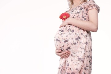 Pregnancy, Motherhood, Mother's Day Holiday concept. Young woman with flowers holds hands on belly.