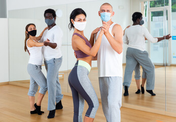 Young adult females and males in masks for disease prevention doing samba partner dance workout during group class in fitness center