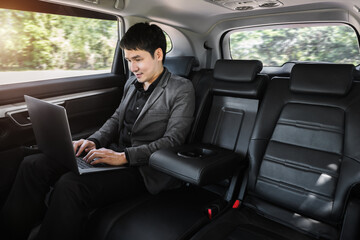 business man using laptop computer while sitting in the back seat of car