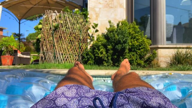 4K slow-motion footage of a guy relaxing on a mat sunbathing in the pool of a large and modern villa of Pozuelo de Alarc&oacute;n, Spain. Concept of luxury neighborhood in Spain.