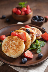 Cottage cheese pancakes or syrniki  with mint, strawberries and blueberries on a dark wooden table. Concept of healthy breakfast. Macro and selective focus image