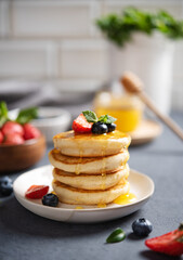 Homemade classic American pancakes in a stack with fresh berries and honey close-up on a blurry white brick background. The concept of a healthy and nutritious breakfast. Vertical orientation