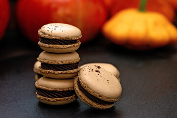 Dessert for Halloween. Thanksgiving menu. French macarons. Macaroons with chocolate on a black background with pumpkins. Soft selective focus. Close up.