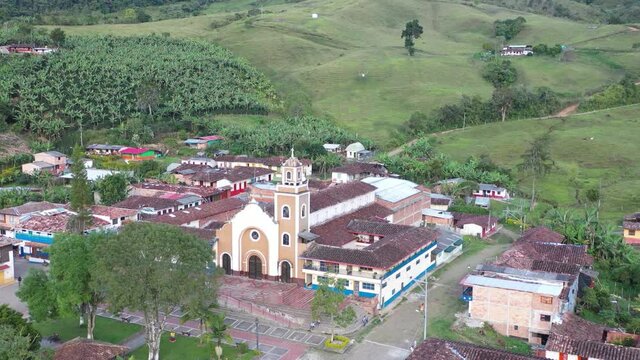 Small traditional village - town in Antioquia Colombia near Andes surrounded by nature, with colorful facades, church in park, small park, clay tiles roofs, cobblestone streets. Drone 4K.