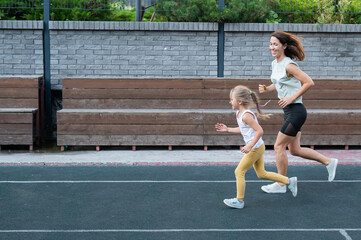 Fototapeta premium Caucasian woman goes in for sports with her daughter outdoors. A schoolgirl and her mother are running around in the stadium.