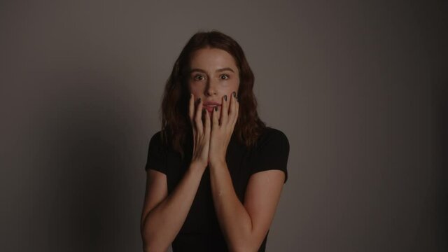 Surprised Woman Expressing Fear With Hands On Her Face In Grey Background.