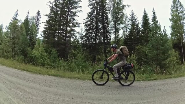 Cyclist hiker rides a bicycle on the road against the background of trees outside the city