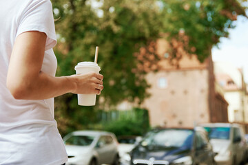 Coffee paper cup in woman hands. Woman drinks coffee to go at city street.