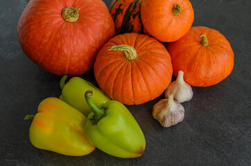 New autumn harvest bright orange pumpkins with green juicy peppers and garlic on text dark background