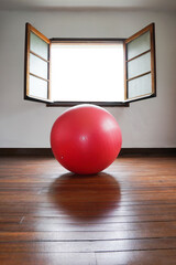 Red pilates swiss ball in a room in front of an opened window. High quality photo