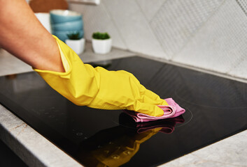 Cleaning induction stove. Woman in yellow rubber gloves cleans kitchen induction hob with cleaning...