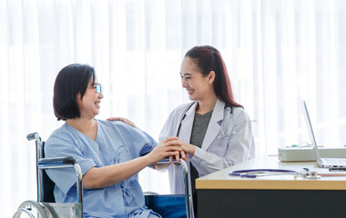 Obraz premium Asian female doctor monitoring checking up senior woman patient on wheelchair while Muslim Arab Islam wears hijab in white lab coat uniform with stethoscope typing information in laptop computer