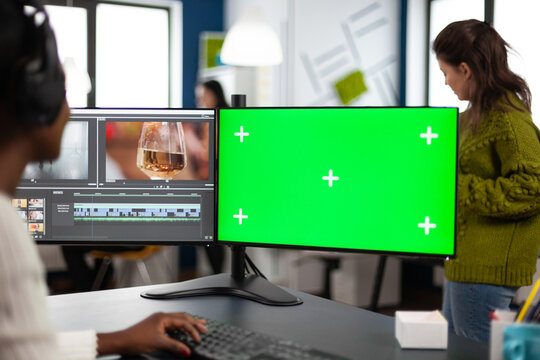 African designer video editor with headset editing footage using pc with greenscreen, chroma key isolated display sitting in agenc company. Videographer in digital multimedia company processing movie