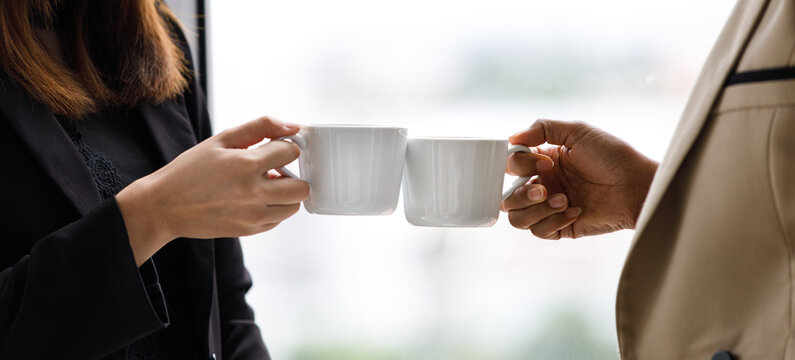 Unidentified unrecognizable businesswoman in casual business clothing standing holding white hot coffee cup clinking cheering toasting celebrating together after successful finish important work