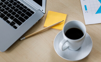 Blank black screen monitor laptop notebook computer for copy space text on working table full of business plan graph chart diagram paperwork report target documents and white coffee cups in office