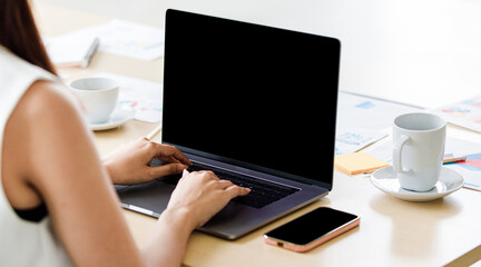 Fototapeta premium Close up shot of black blank screen monitor laptop notebook computer on working table with paperwork documents while unidentified unrecognizable female professional secretary typing on keyboard