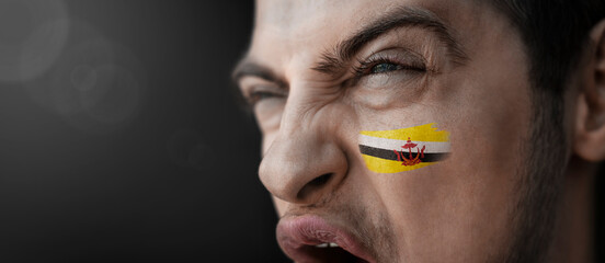 A screaming man with the image of the Brunei national flag on his face