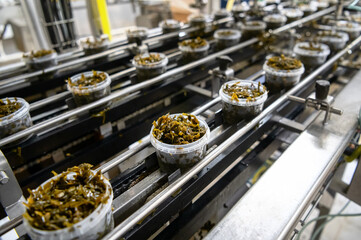 Seaweed salad in plastic jars on a conveyor belt. Automatic line for packing seafood