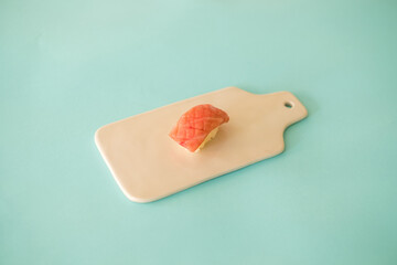 Sushi Nigiri with raw tuna served on white board. One sushi piece on the white tray isolated on turquoise background. Japanese traditional food. 