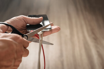 Closeup photo of mans hand with scissors cutting smartphone usb wire