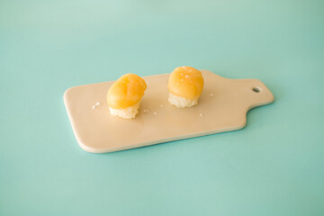 Two Nigiri Sushi with scallop served on beige board. Two sushi pieces served on the creamy tray isolated on turquoise background. Japanese food. 