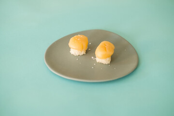 Two Nigiri Sushi with scallop served on light grey plate. Two sushi pieces served on the plate isolated on turquoise background. Japanese food. 