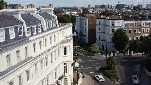 Aerial view of cars driving through street intersection. Tilt down fly over corner of big white building in urban neighbourhood. London, UK