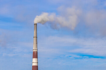 A smoking pipe of a power plant against the background of a blue sky with clouds. The concept of environmental pollution. The problem of ecology.
