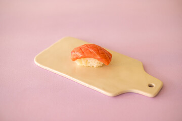 Sushi Nigiri with raw tuna served on white board. One sushi piece on the white tray isolated on pink background. Japanese traditional food. 