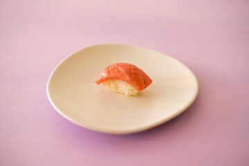 Sushi Nigiri with raw tuna served on white plate. One sushi piece on the white plate isolated on pink background. Japanese traditional food. 