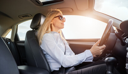 Fototapeta na wymiar Side view of positive mature lady in sunglasses and formal clothes driving modern car by herself. Concept of people, confident and experienced driver.