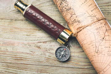 Old spyglass and compass with vintage world map on wooden background