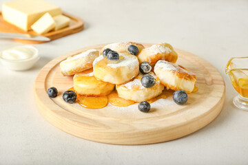 Board with tasty cottage cheese pancakes, powdered sugar, blueberry and honey on table