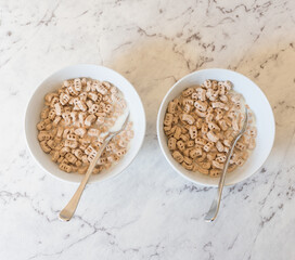 High angle view of two bowls of gluten free cereal with milk and spoon on bench (selective focus)