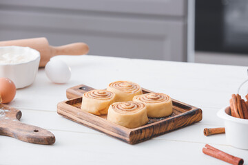 Board with uncooked cinnamon rolls on table in kitchen