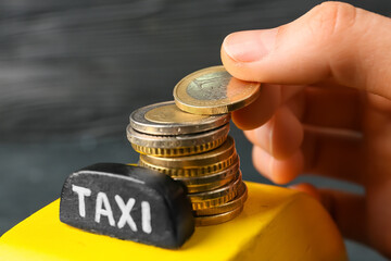 Female hand with yellow cab and coins on dark background, closeup