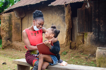 An African mother or teacher outside a village mud house with nose mask, helping a girl child with her studies for excellence in her school, career and education