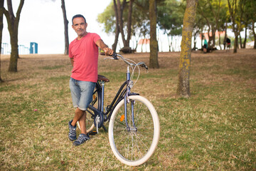 Fototapeta na wymiar Portrait of happy mature man standing at his bike. Man posing with bicycle in park. Active seniors concept