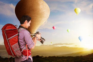 Asian man with backpack and camera looking at colorful air balloon flying
