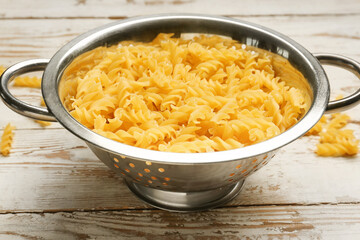 Colander with uncooked fusilli pasta on wooden background