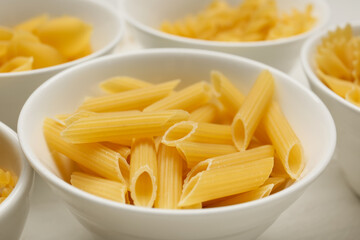 Bowl with uncooked penne pasta on white wooden background
