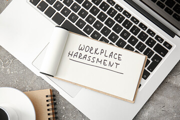 Notebook with text WORKPLACE HARASSMENT and laptop on grunge background