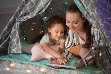 Mother with her little daughter reading bedtime story in play tent at home