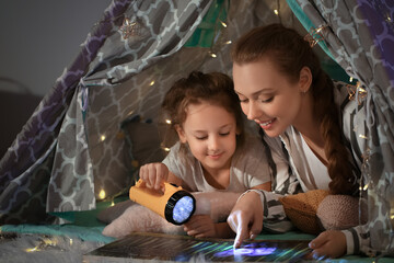 Mother with her little daughter reading fairy-tale in play tent at home