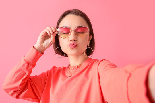 Beautiful young woman blowing kiss on pink background