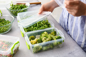 Woman closing plastic containers with frozen vegetables at table in kitchen, closeup