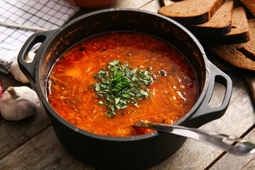 Cooking pot with delicious borscht and greens on wooden table